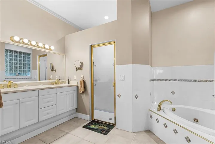 Bathroom featuring double vanity, a whirlpool tub, light tile patterned flooring, and a shower stall