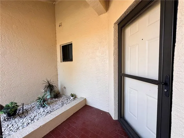 Entryway with textured stucco walls, a red-hued tile floor, and a white panel door featuring a black security screen