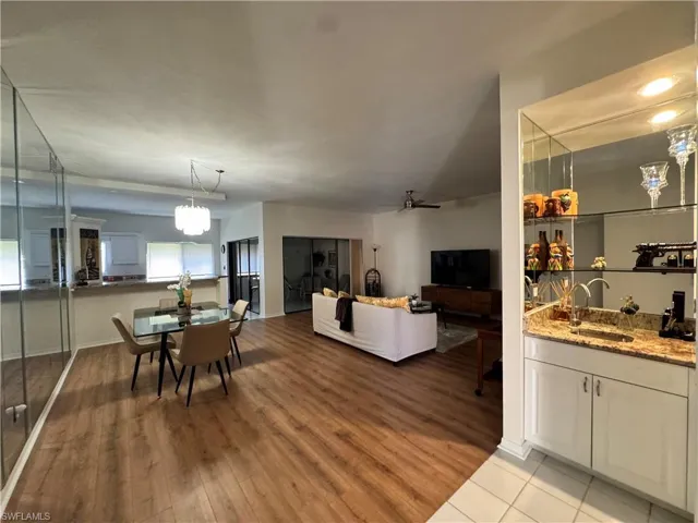 Open-concept living space featuring wood-finish flooring, a contemporary chandelier, a built-in wet bar with a granite-style countertop, and mirrored wall accents