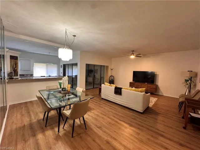 Open-concept living area featuring wood-finish flooring, a contemporary dining chandelier, and a breakfast bar with a stone-look countertop
