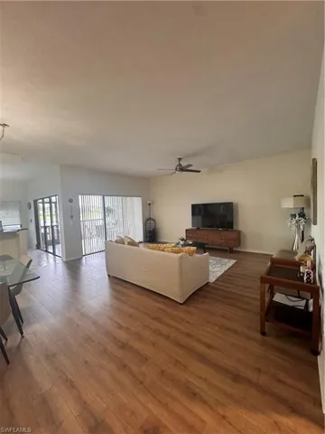 This spacious living area features wood-look flooring and a ceiling fan, offering direct access to an outdoor screened area through sliding glass doors