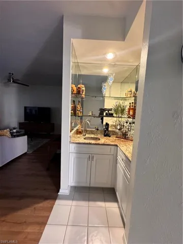 Built-in wet bar featuring a speckled countertop, white cabinetry, undermount sink, and mirrored shelving with recessed lighting