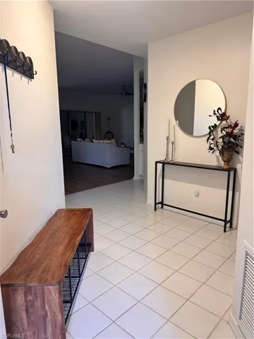 Entryway featuring light-colored square tile flooring and a view into an interior living space with dark wood flooring