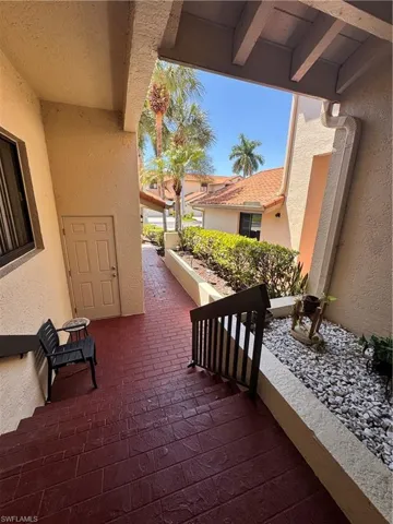 Entryway featuring stamped brick-patterned flooring, a black metal handrail, stucco exterior walls, and a landscaped rock garden
