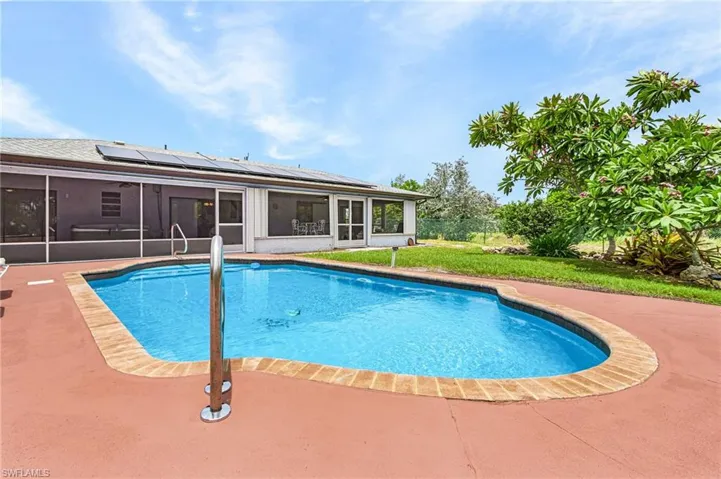 Freeform swimming pool with a red-toned concrete deck, brick-patterned coping, and a stainless steel handrail