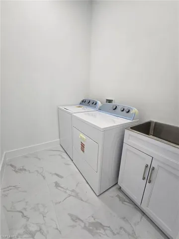 Washroom with light marble finish flooring, washer and clothes dryer, and cabinet space