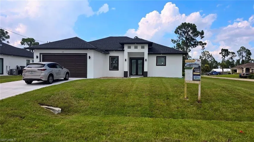 Prairie-style house featuring stucco siding, an attached garage, a front lawn, and driveway