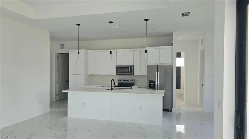 Kitchen with white cabinetry, light marble finish floors, an island with sink, and stainless steel appliances