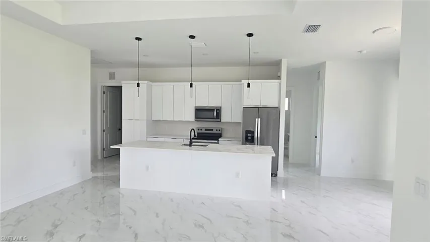 Kitchen with white cabinets, a center island with sink, light marble finish floors, light countertops, and appliances with stainless steel finishes