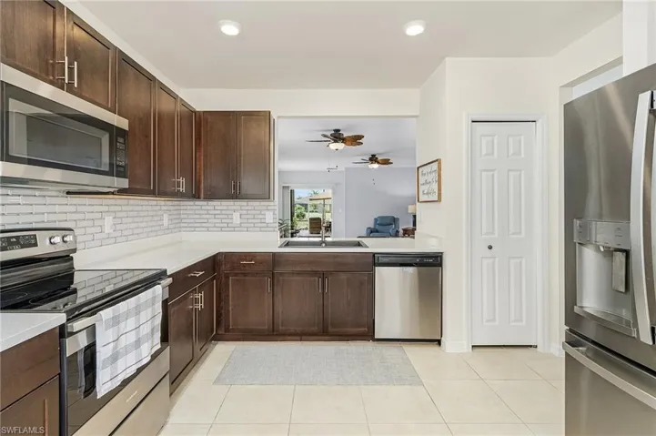 Kitchen featuring dark brown cabinets, ceiling fan, light tile flooring, backsplash, and appliances with stainless steel finishes