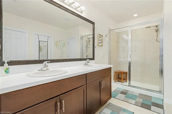 Bathroom with tile floors, vanity with extensive cabinet space, an enclosed shower, and double sink