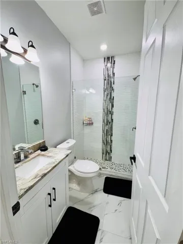 Full bath with vanity, a shower stall, marble look tiles, and recessed lighting