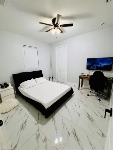 Bedroom featuring light marble finish floors, a ceiling fan, and a desk