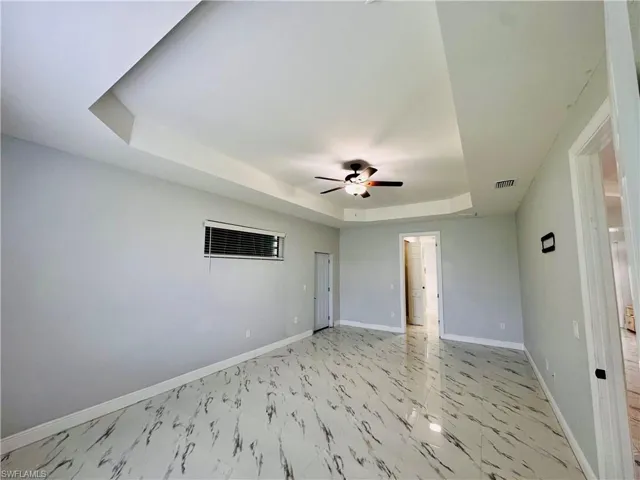 Spare room featuring a tray ceiling, light marble finish floors, and a ceiling fan