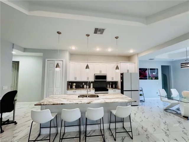 Kitchen featuring decorative light fixtures, light stone counters, decorative backsplash, freestanding refrigerator, and recessed lighting