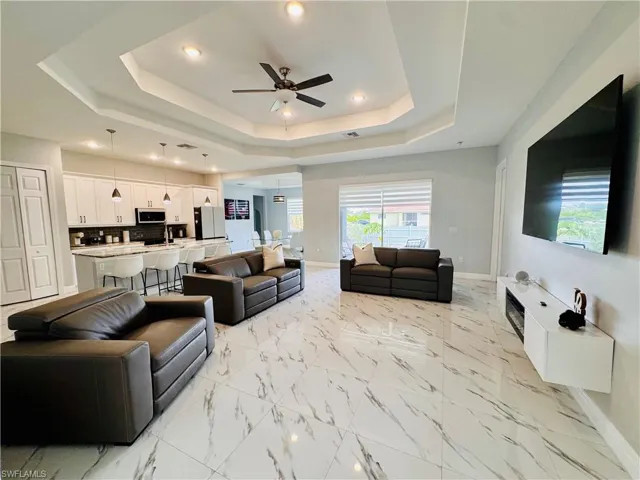 Living room with a ceiling fan, light marble finish floors, a tray ceiling, and recessed lighting