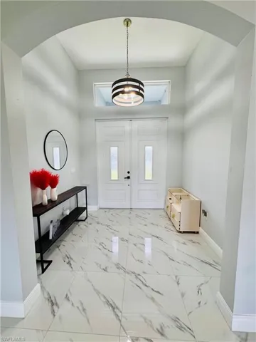 Foyer with plenty of natural light, light marble finish floors, and a chandelier
