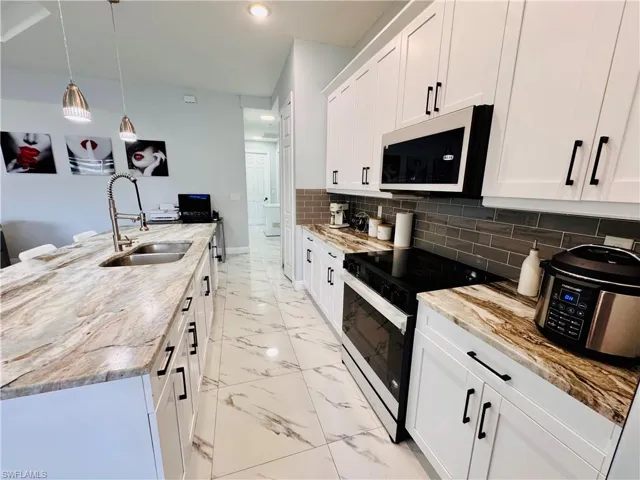 Kitchen with black / electric stove, white cabinets, hanging light fixtures, white microwave, and tasteful backsplash