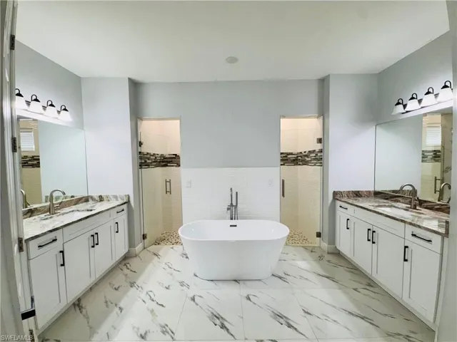 Bathroom with a shower stall, a freestanding bath, tile walls, and two vanities