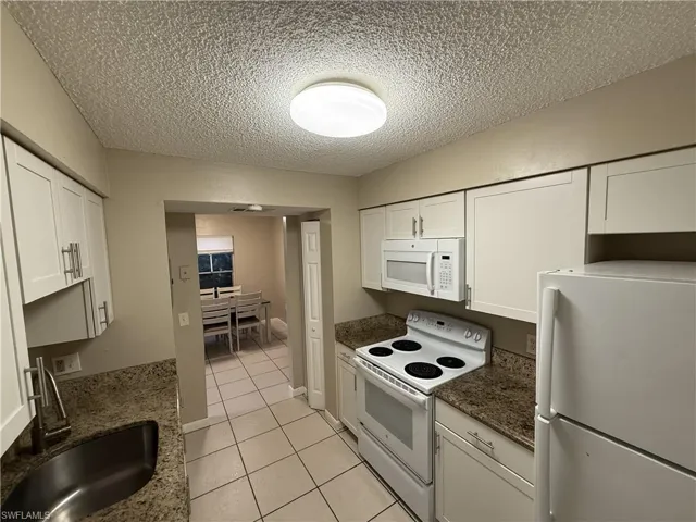 Kitchen featuring a textured ceiling, white cabinetry, sink, and white appliances