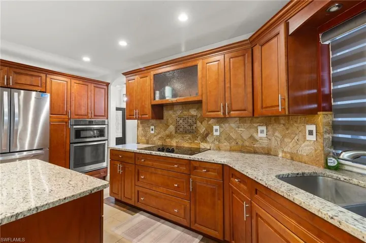 Kitchen with light stone counters, backsplash, and appliances with stainless steel finishes