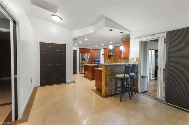 Kitchen with stainless steel fridge with ice dispenser, lofted ceiling, a breakfast bar, tasteful backsplash, and light tile floors