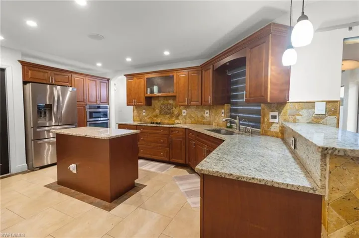 Kitchen with a center island, appliances with stainless steel finishes, decorative light fixtures, backsplash, and light tile floors