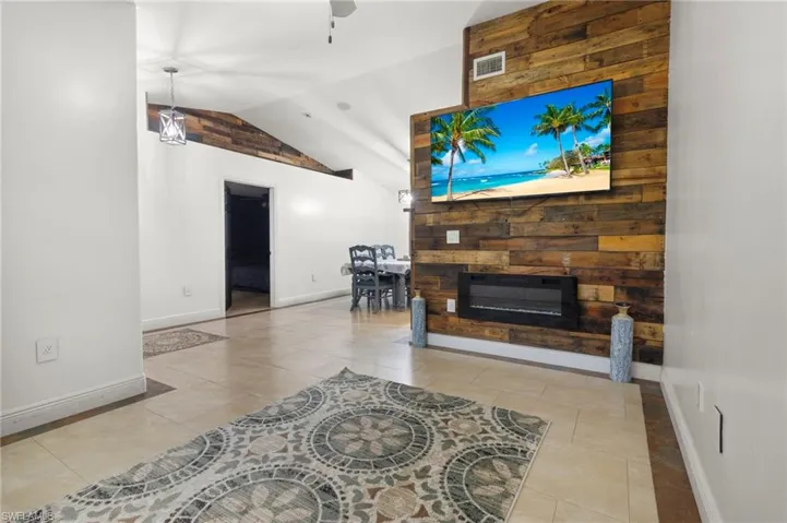 Tiled living room featuring vaulted ceiling, wooden walls, and ceiling fan