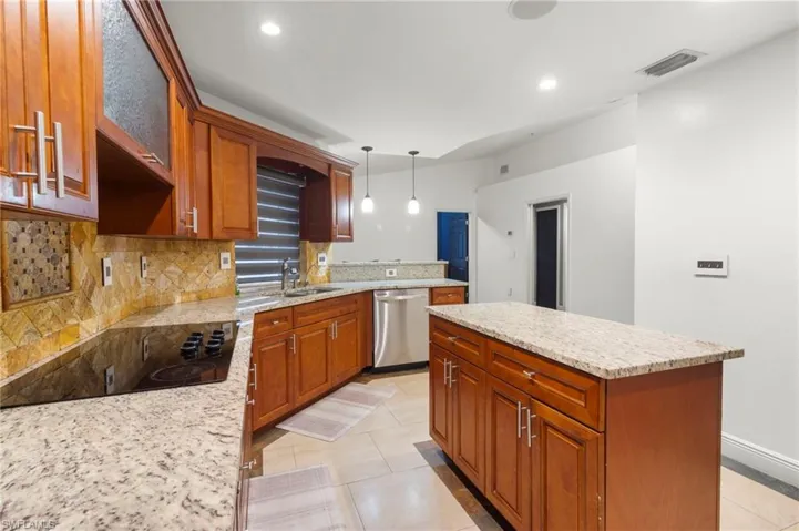 Kitchen with light tile flooring, backsplash, hanging light fixtures, a center island, and stainless steel dishwasher