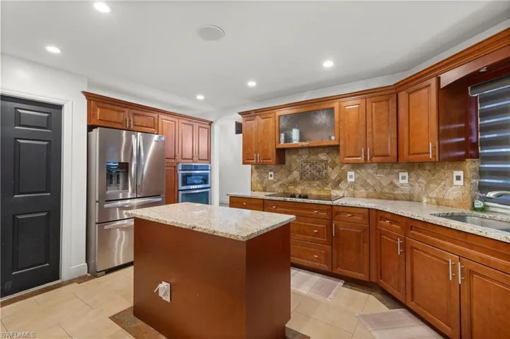 Kitchen with light stone countertops, a kitchen island, backsplash, light tile floors, and appliances with stainless steel finishes