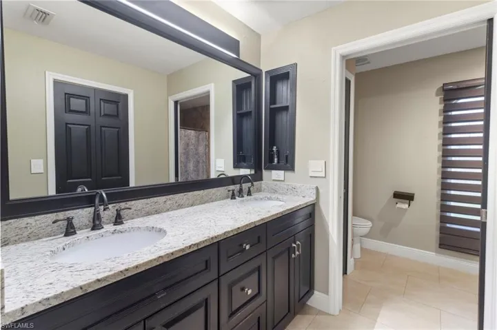 Bathroom featuring tile floors, large vanity, toilet, and double sink