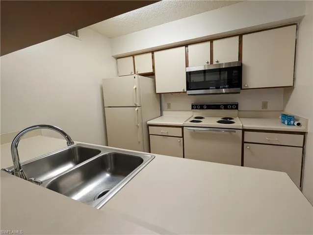 Kitchen with light countertops, white appliances, white cabinetry, and a textured ceiling