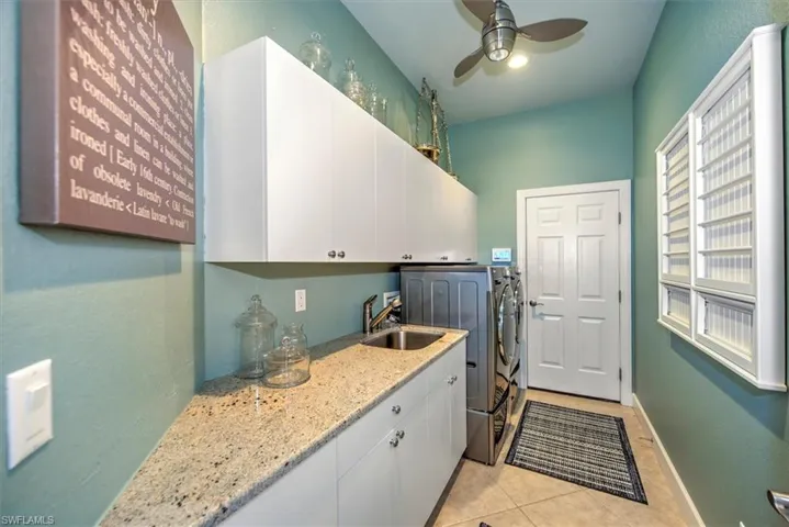 Laundry room featuring cabinets, light tile patterned flooring, sink, ceiling fan, and washer and clothes dryer