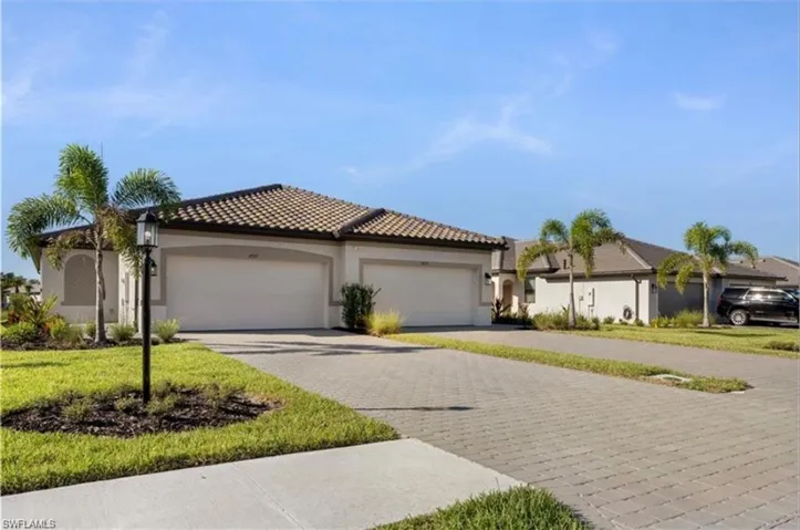 View of front facade with decorative driveway, stucco siding, a tile roof, and a front lawn