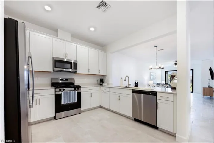 Kitchen featuring appliances with stainless steel finishes, white cabinets, a chandelier, pendant lighting, and recessed lighting