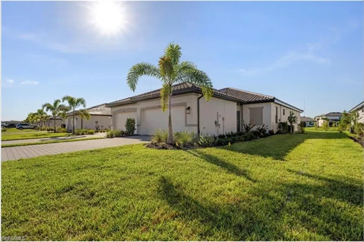 View of side of property with a lawn, decorative driveway, a garage, stucco siding, and a tile roof