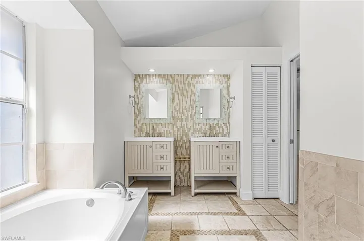 Bathroom featuring a closet, vanity, tile walls, healthy amount of natural light, and a garden tub