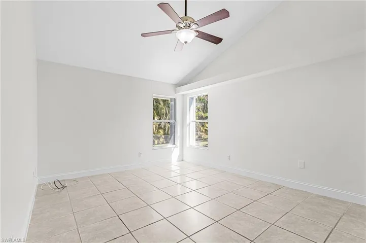 Unfurnished room with lofted ceiling, ceiling fan, and light tile patterned floors