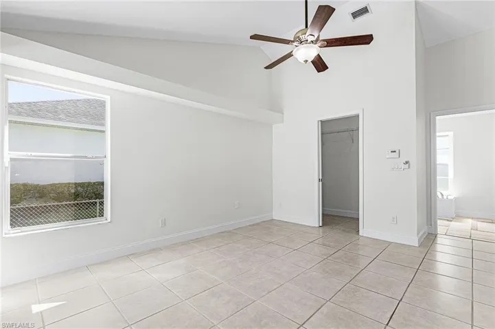 Unfurnished bedroom featuring a walk in closet, vaulted ceiling, ceiling fan, multiple windows, and light tile patterned floors