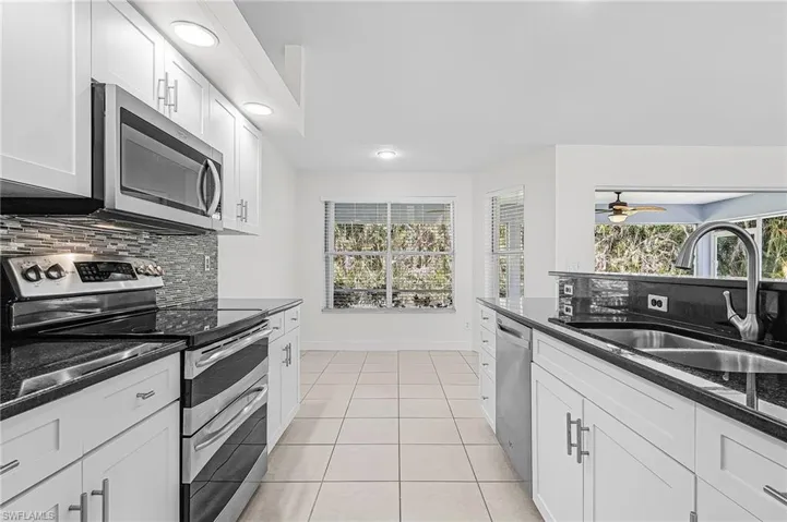 Kitchen with stainless steel appliances, tasteful backsplash, dark stone counters, white cabinetry, and light tile patterned floors