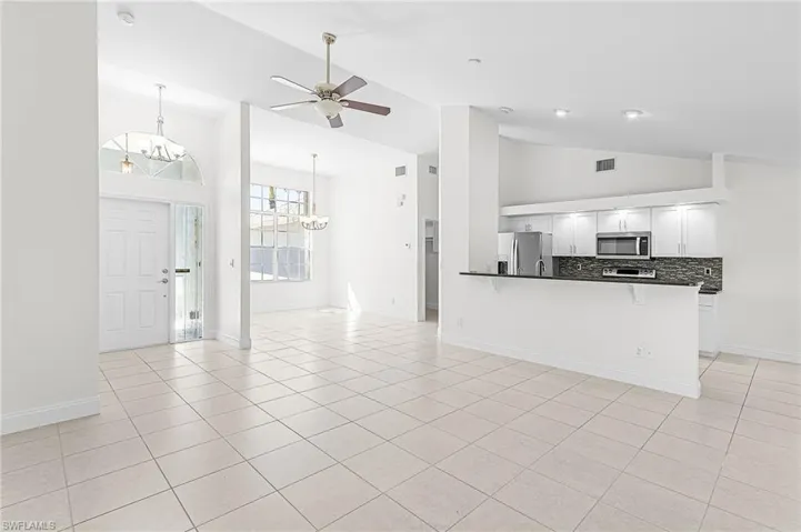 Unfurnished living room featuring a chandelier, ceiling fan, light tile patterned flooring, and lofted ceiling