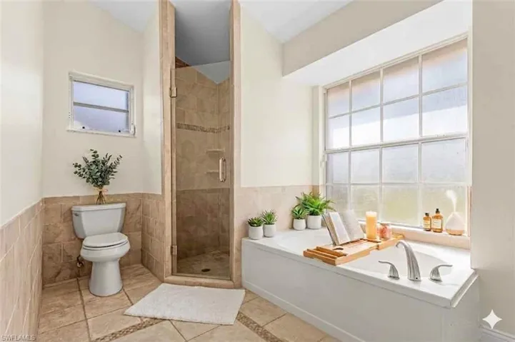 virtual staged Bathroom with a garden tub, a shower stall, light tile patterned floors, tile walls, and wainscoting