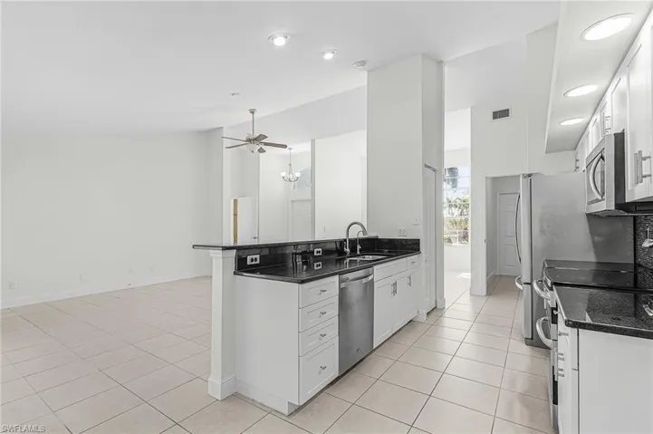 Kitchen with white cabinets, stainless steel appliances, dark stone countertops, light tile patterned flooring, and lofted ceiling
