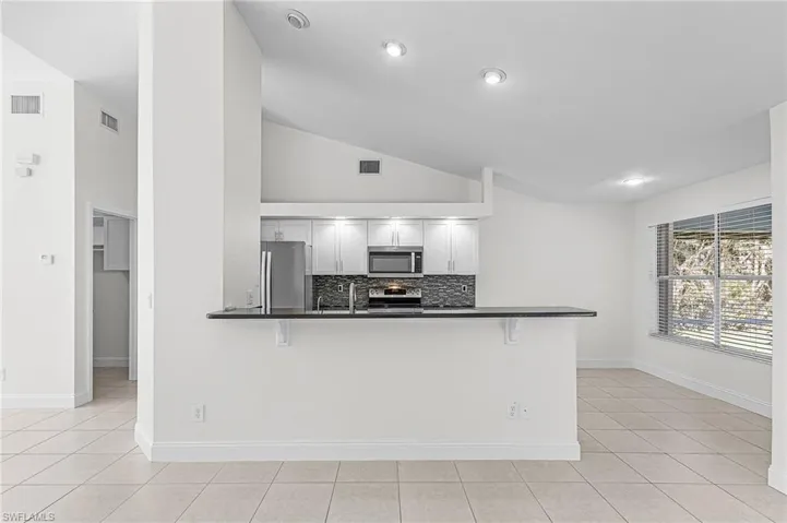 Kitchen featuring a breakfast bar, stainless steel appliances, tasteful backsplash, lofted ceiling, and a peninsula