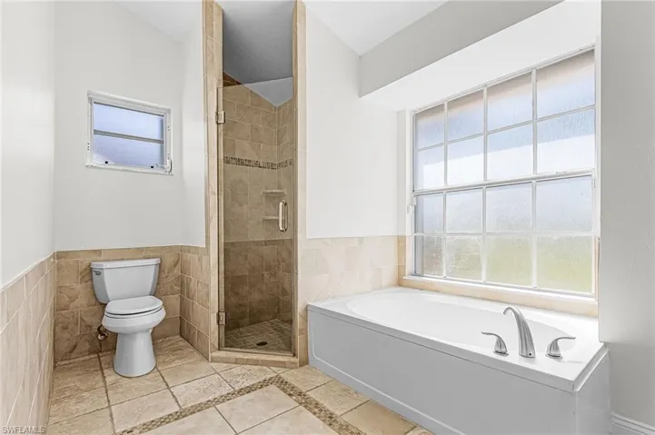 Bathroom with a bath, a shower stall, tile walls, a wainscoted wall, and light tile patterned flooring