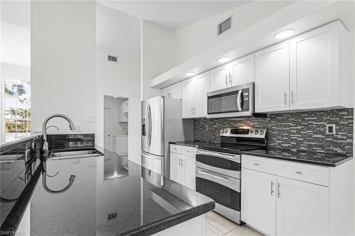 Kitchen with dark stone counters, stainless steel appliances, white cabinetry, a high ceiling, and backsplash
