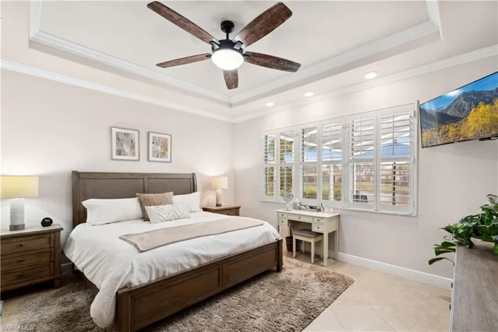 Tiled bedroom with a raised ceiling, ceiling fan, and ornamental molding