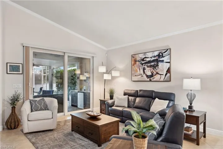 Living room with light tile patterned floors, ornamental molding, and vaulted ceiling