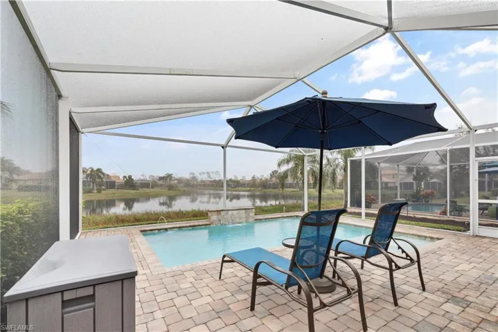 View of pool featuring pool water feature, a patio, a water view, and glass enclosure