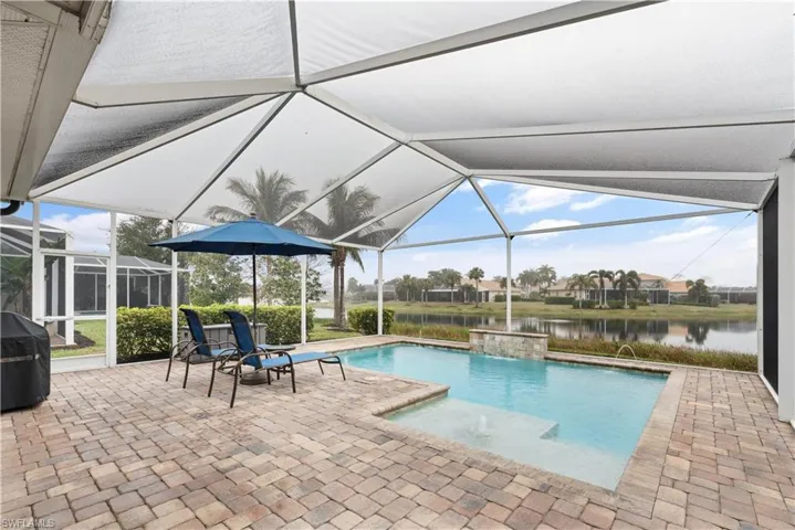 View of swimming pool with a lanai, a grill, pool water feature, a water view, and a patio
